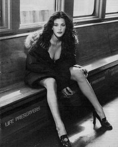 a black and white photo of a woman sitting on a train bench with her legs crossed