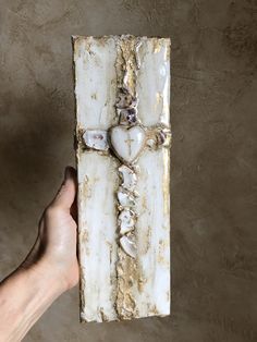 a hand holding up a cross made out of shells