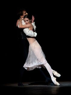 two people are dancing in the dark with their arms around each other and one is wearing a white dress