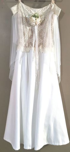 a white dress hanging up on a clothes hanger with lace and flowers attached to it