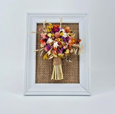 a bouquet of flowers in a white frame on a burlap background is displayed