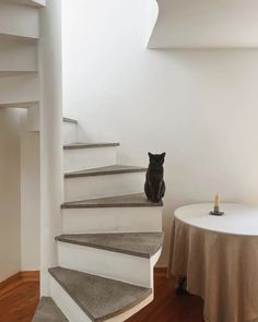 a black cat sitting on top of a set of stairs next to a white table