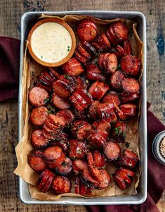 a tray filled with cooked sausages next to a bowl of dipping sauce