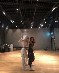 two women standing in an empty room with lights on the ceiling and wood flooring