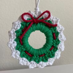 a crocheted christmas ornament hanging on a wall with a red ribbon