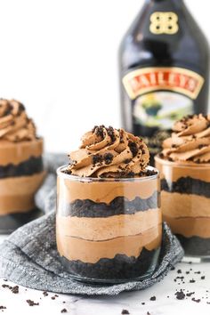 three dessert cups with chocolate frosting and oreo cookies in front of a bottle of booze