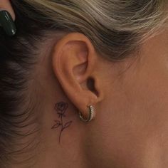 a woman's ear has a small rose tattoo on it