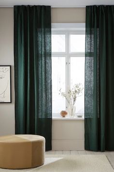 a living room with green curtains and a round ottoman in front of a large window