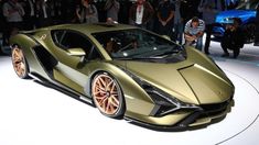 a gold colored sports car on display at an auto show with people standing around it