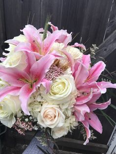 a vase filled with pink and white flowers on top of a wooden table next to a fence