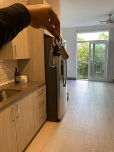 a person is holding keys to a refrigerator in a room with wood floors and white cabinets