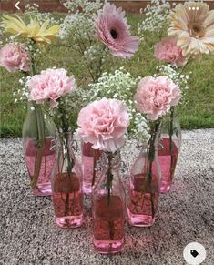 pink and yellow flowers are in glass vases on the ground with grass behind them