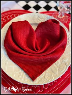 a heart - shaped napkin sits on top of a red and white plate with silverware