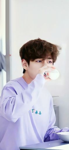 a young man is brushing his teeth while sitting at a table in front of a laptop computer