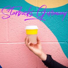 a person holding a cup in front of a wall with the words starbucks giveaway written on it