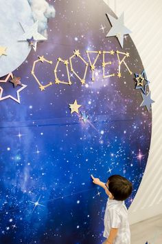 a young boy is painting the word couver in front of a blue background with stars