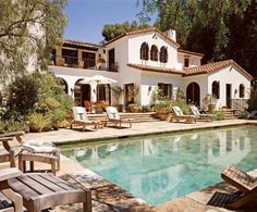 a house with a pool in front of it and lawn chairs around the pool area