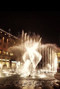 there is a fountain that has water shooting out of it and lights in the background