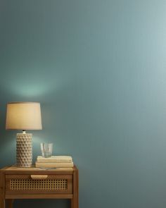 a small table with a lamp on it next to a blue wall and some books