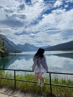 a woman leaning on a rail next to a body of water with mountains in the background