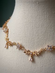 a gold necklace on a mannequin is adorned with crystal beads and leaves,