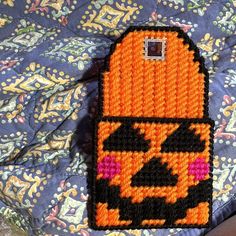 a knitted cell phone case sitting on top of a bed covered in blue and orange fabric