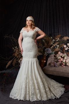 a woman in a white wedding dress standing next to a couch and flower bouquets