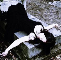 a woman laying on top of a cement bench