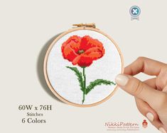 a hand is holding a small cross stitched orange flower in front of a white background