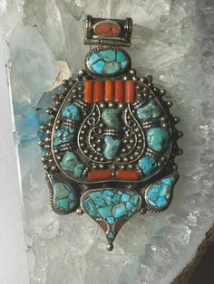 Beautiful/interesting old handmade white brass pandant with inlaid stones coral & torquise from Tibet.Beautiful shaped & great condition. Measurements:- Height - 2.9 inches  Width - 1.7 inches  Thickness - 0.3 inches  Weight-38 grams  * Colors may vary slightly  in person due to the lighting/flash lighting in photo shoots. Traditional Turquoise Pendant Necklace With Natural Stones, Traditional Turquoise Inlay Necklace As Gift, Traditional Handmade Turquoise Pendant Necklace, Traditional Turquoise Necklace With Inlay For Gift, Traditional Turquoise Pendant Necklace, Unique Turquoise Pendant Necklace, Unique Turquoise Stone Pendant Necklace, Unique Turquoise Pendant Necklace With Stones, Antique Turquoise Pendant Necklace