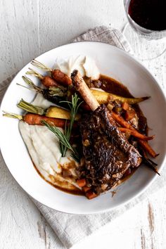 a white plate topped with meat and veggies on top of mashed potatoes