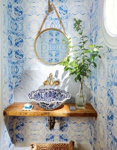 a bathroom with blue and white wallpaper, a round mirror and a bowl sink