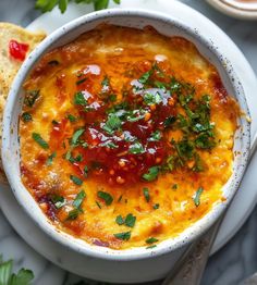 a white bowl filled with food on top of a plate next to bread and garnish