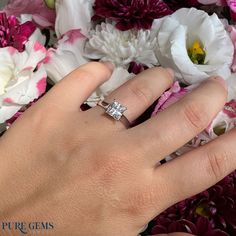 a woman's hand with a diamond ring on it and flowers in the background