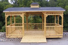 a wooden gazebo sitting on top of a gravel covered ground next to trees and bushes