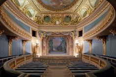 an ornately decorated auditorium with blue seats and gold trim around the walls, along with a painting on the wall