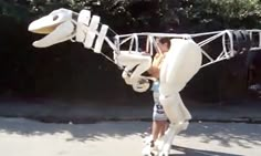 a man in a white suit is holding up a fake dinosaur like object that looks like a boat