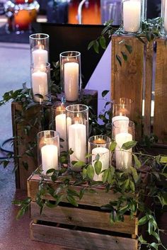 candles are arranged in glass vases with greenery on the sides and around them