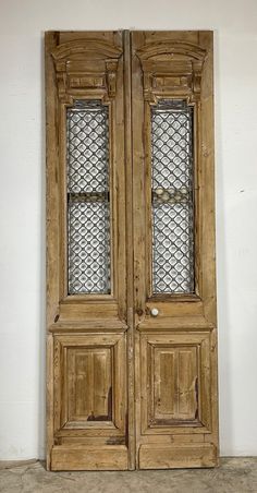 an old wooden double door with glass inserts on the top and bottom panels, in front of a white wall