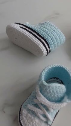 two crocheted baby shoes sitting on top of a white table next to each other