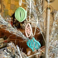 some ornaments are hanging from a tree with tinsel on it and one has a monogram ornament