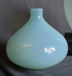 a light blue vase sitting on top of a table next to a black and white clock