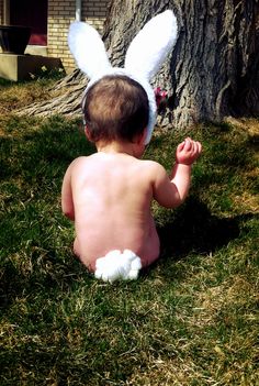 a baby sitting in the grass with an easter bunny ears on it's head