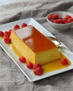 a piece of cake on a white plate with raspberries and syrup in the background