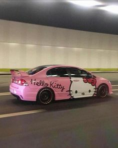 a pink car with hello kitty decals on it's hood driving down the street