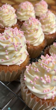 cupcakes with white frosting and pink sprinkles on a cooling rack