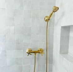 a gold shower head and handset in a white tiled bathroom