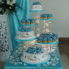 a blue and white wedding cake with cupcakes on it