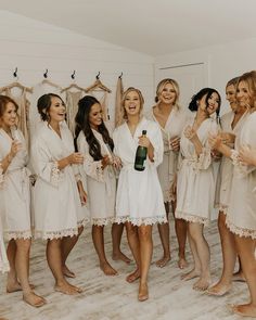 a group of women standing next to each other in robes holding champagne bottles and smiling