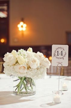 a vase filled with white flowers sitting on top of a table next to a sign